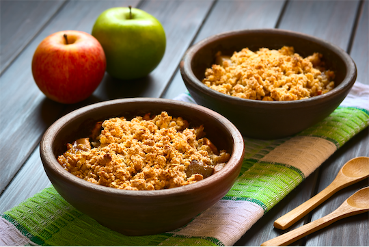 apple crisp in wooden bowls set on top of a towel with wooden spoons next to it